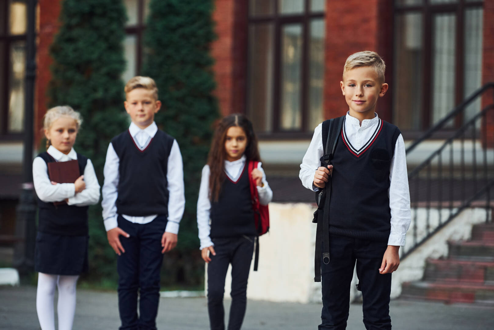 Group of kids in school uniform posing to the camera outdoors together near education building.